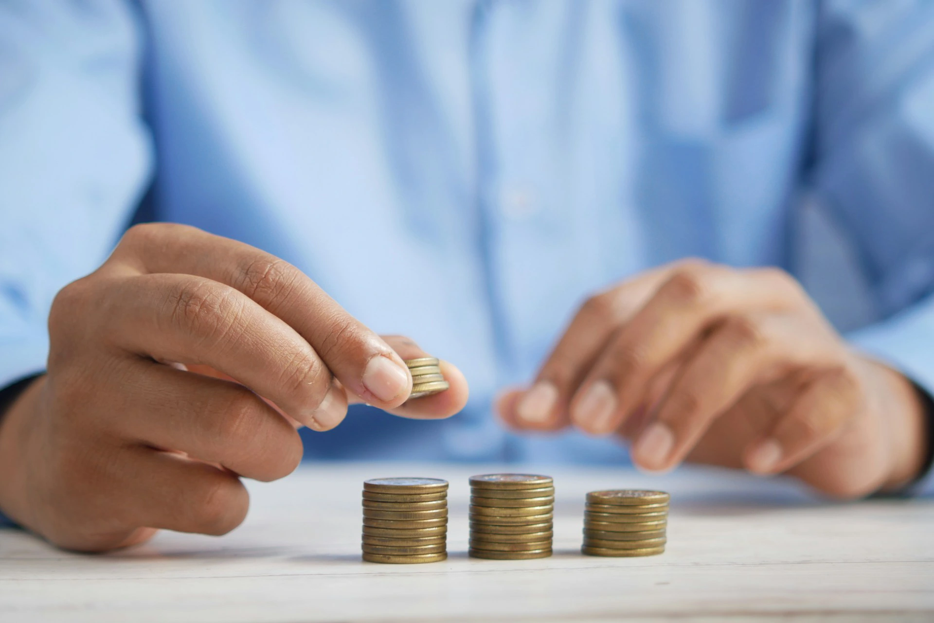 Person in blue shirt stacking coins on a white table.