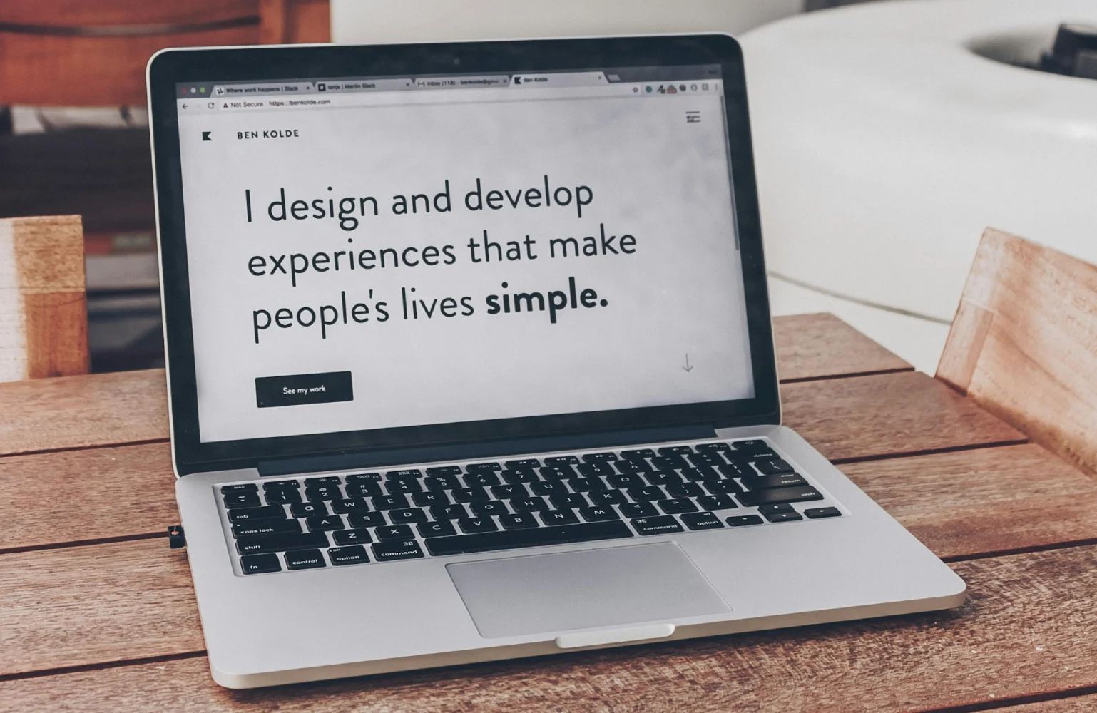 Silver laptop displaying a minimalist personal website with the headline "I design and develop experiences that make people's lives simple" resting on a wooden slatted table.
