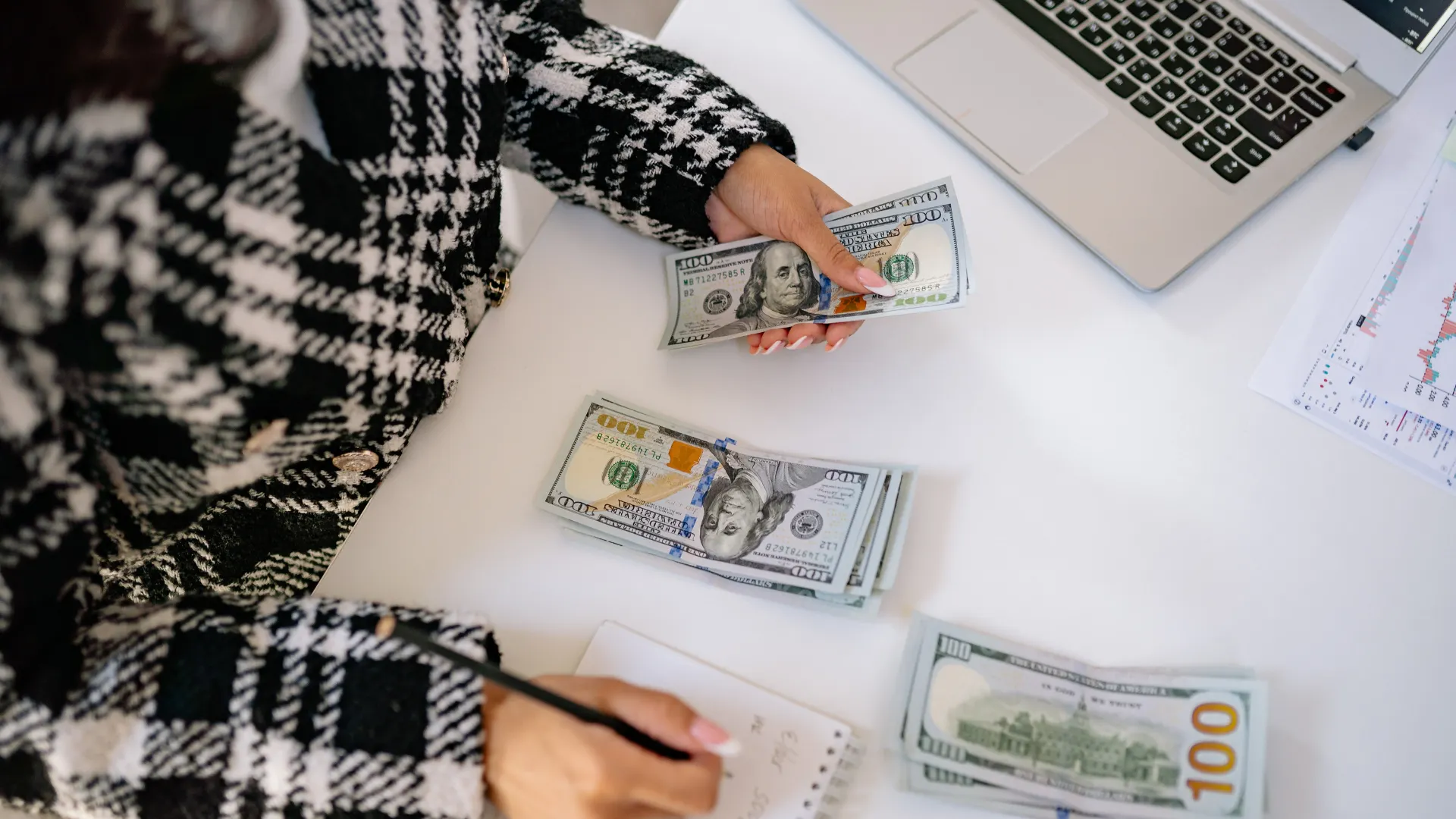 A woman counting money with a laptop beside her.