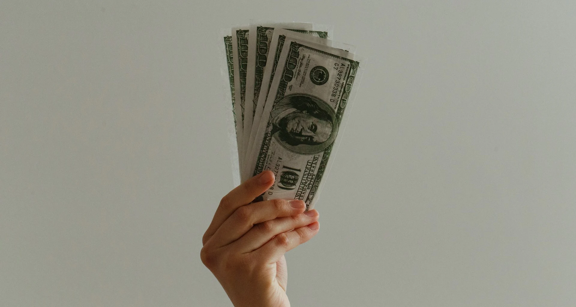 Hand holds a fan of US $100 bills against a plain background.