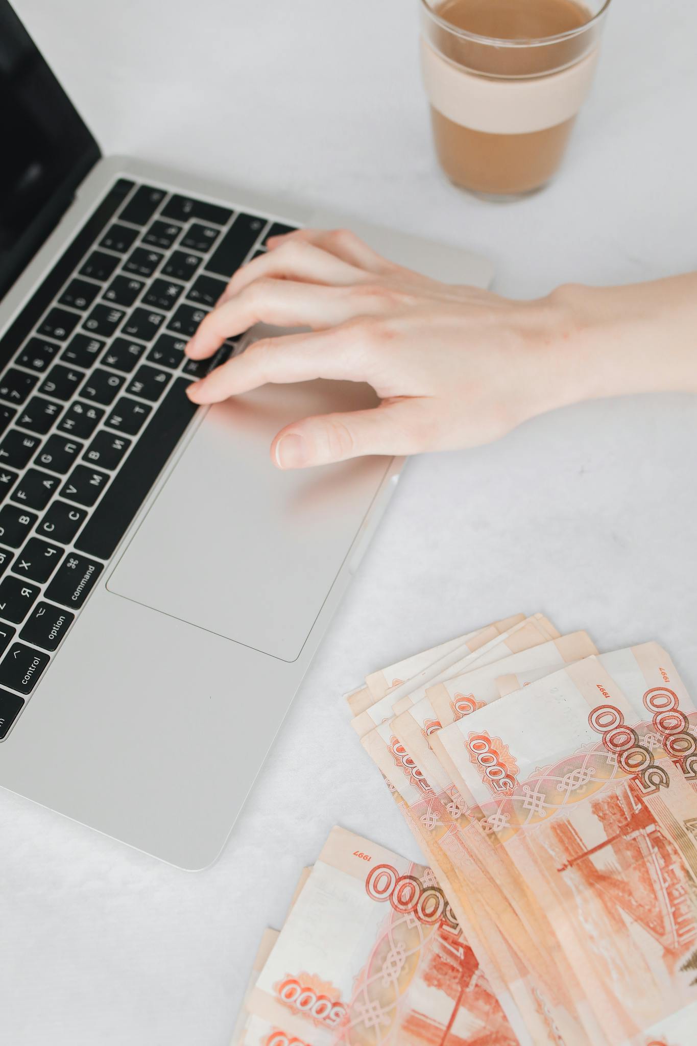 A person browsing websites that pay on a laptop next to a stack of Russian Rubles on a white table.