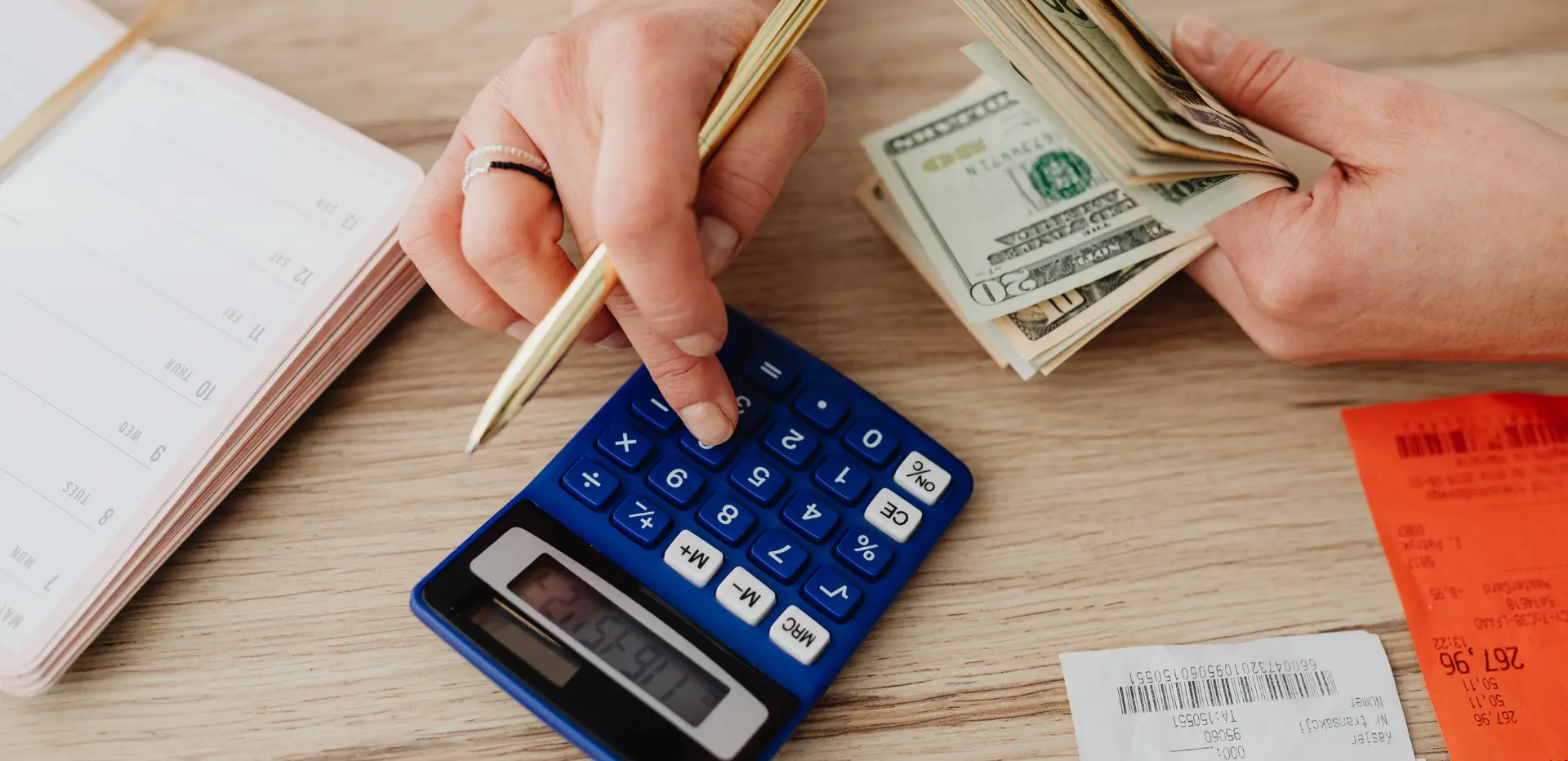 Hand holding money and another one dialing a calculator.