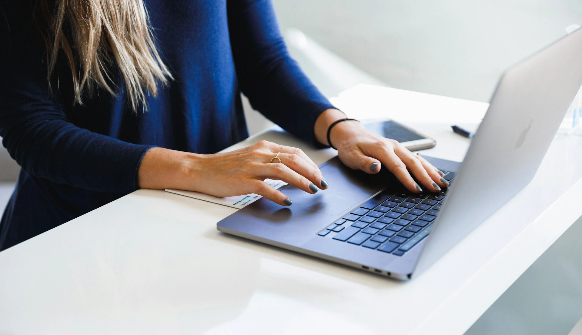 Close-up of a woman's hands typing on a laptop keyboard at a white desk.