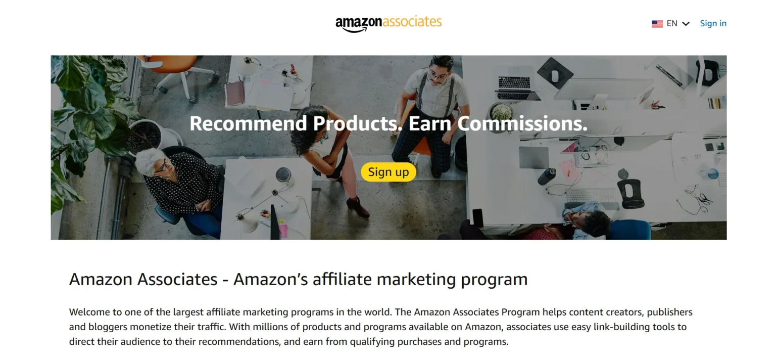 Amazon Associates landing page featuring an overhead view of diverse people collaborating around desks with the text "Recommend Products. Earn Commissions." and a "Sign up" button.
