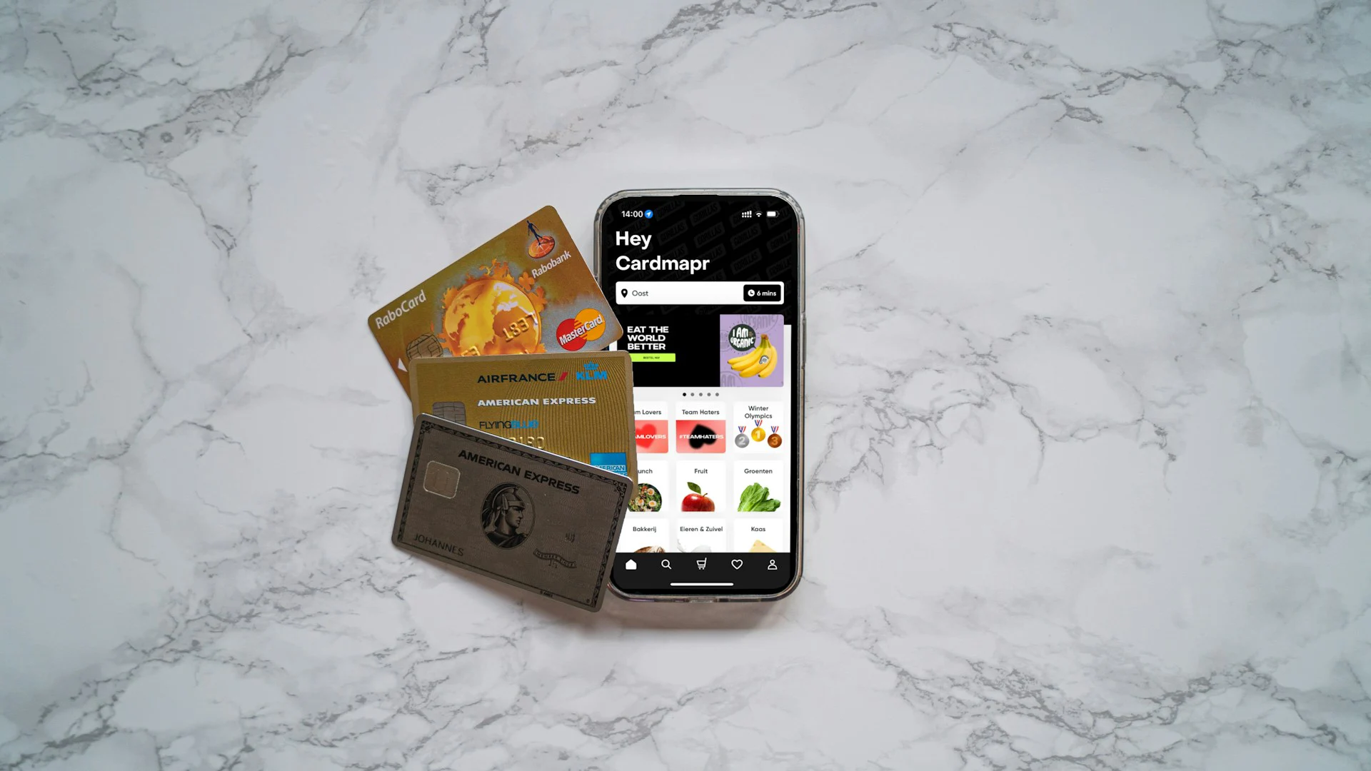 Smartphone displaying a shopping app next to a stack of three credit cards on a white marble surface.