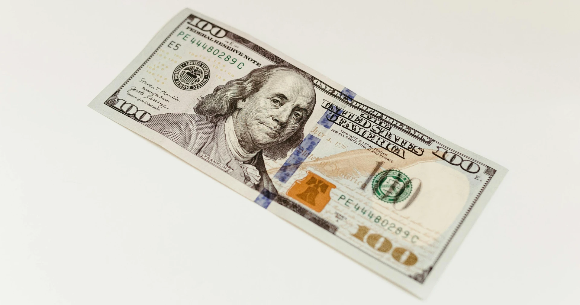 One contemporary United States one hundred dollar bill featuring Benjamin Franklin is angled diagonally against a plain white background.