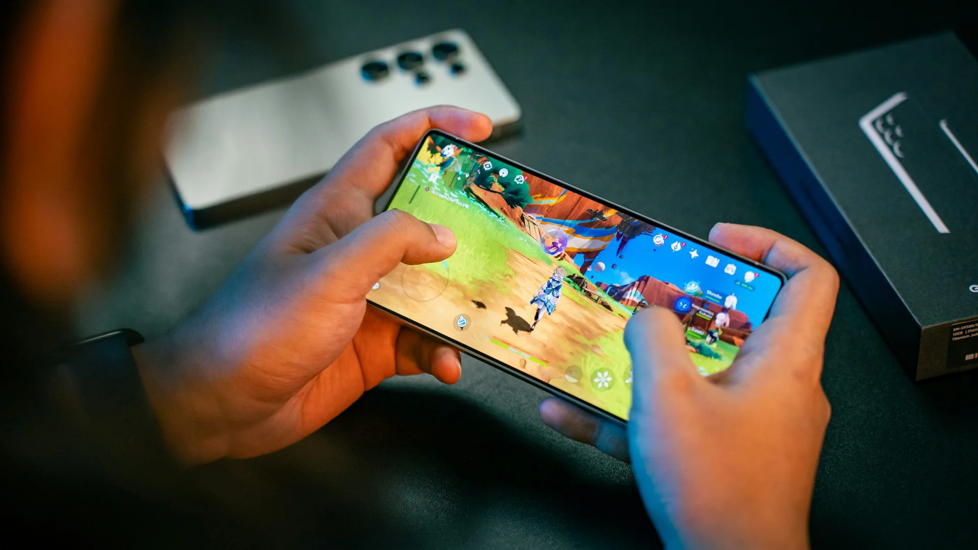 Two hands holding a smartphone horizontally while playing a vibrant 3D adventure game, with a second phone and its packaging visible in the background.