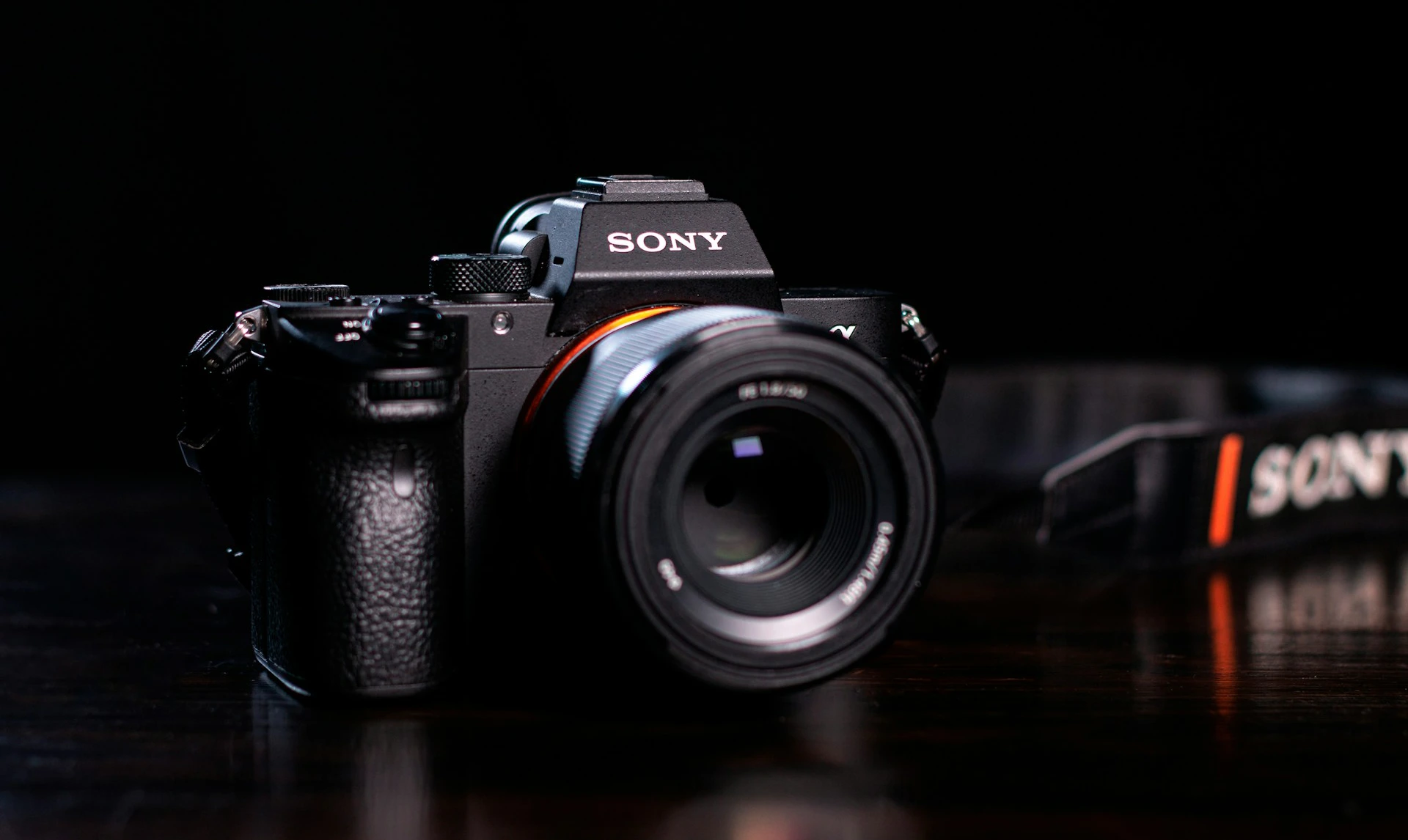 Sony mirrorless camera with a lens attached, resting on a dark surface with a Sony camera strap in the background.
