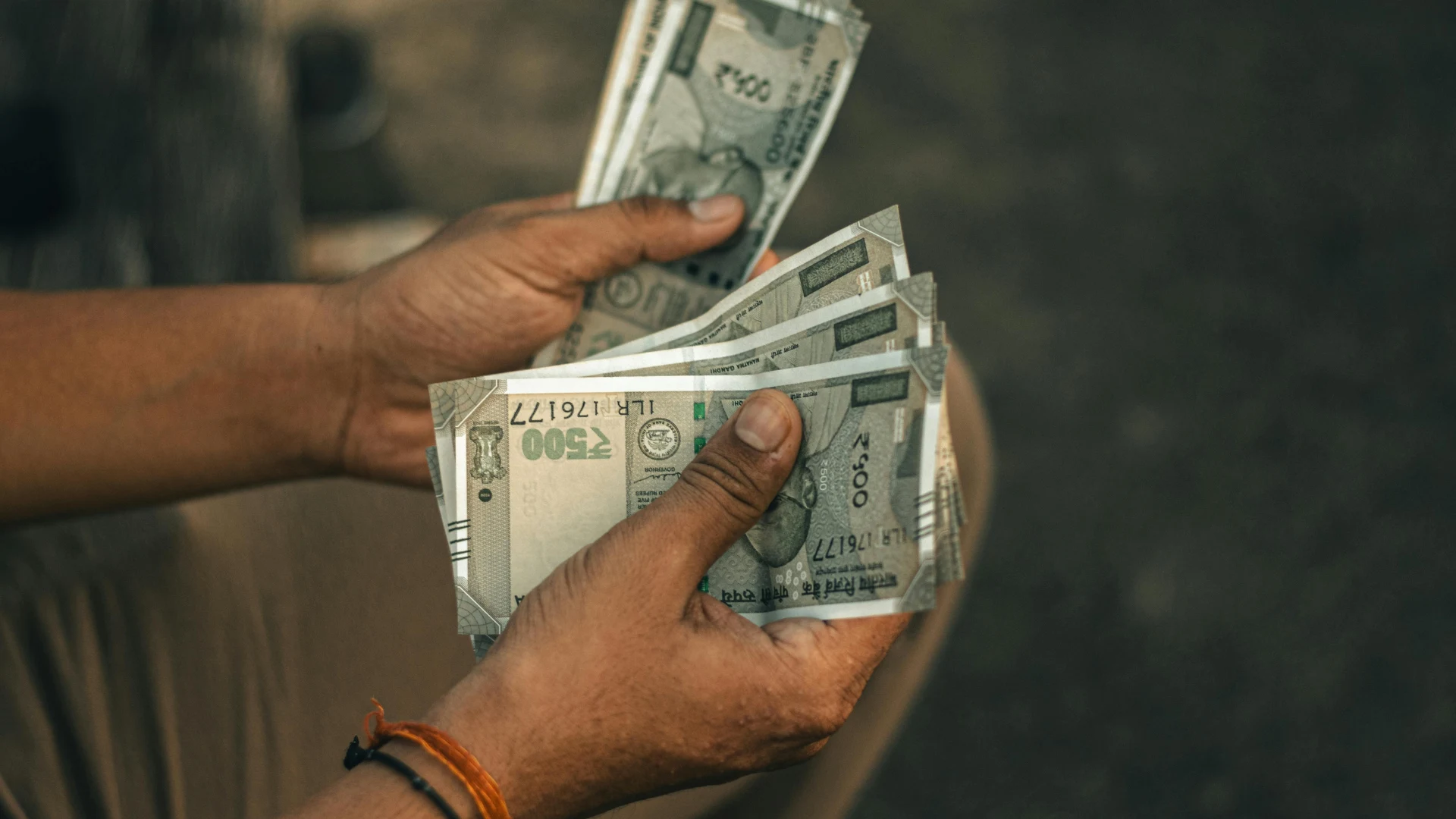 Hands hold several ₹500 Indian rupee banknotes.