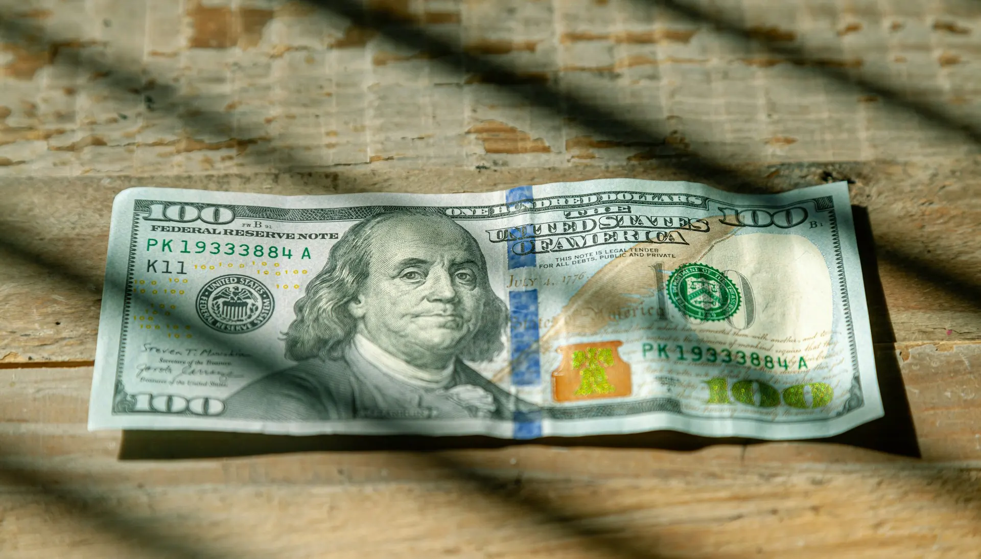A close-up of a crumpled US one hundred dollar bill featuring Benjamin Franklin on a wooden surface.