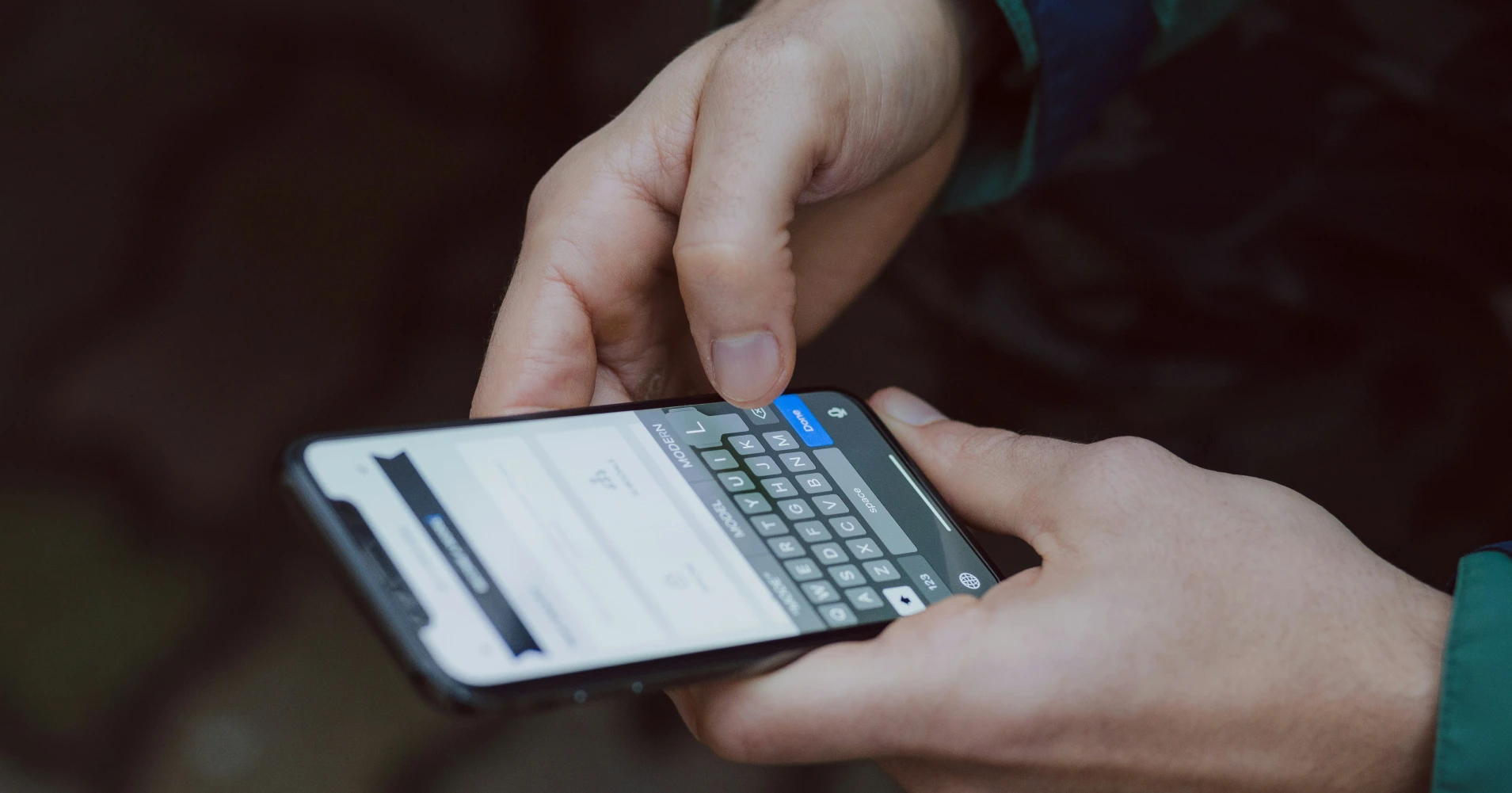Close-up of hands holding and typing on a smartphone with a blurred office background.