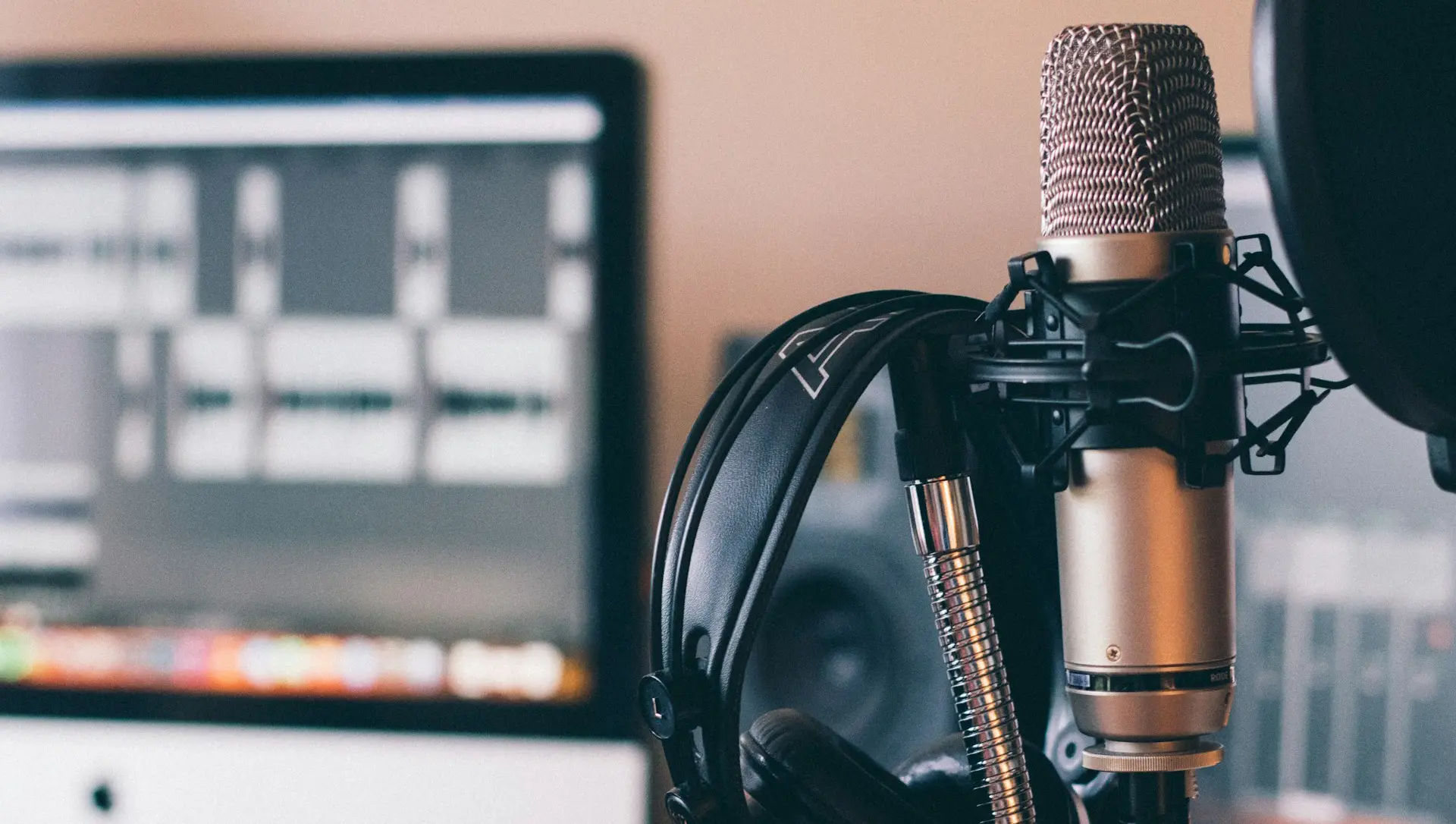 Recording studio setup with a microphone, headphones, and computer monitor displaying audio waveforms.