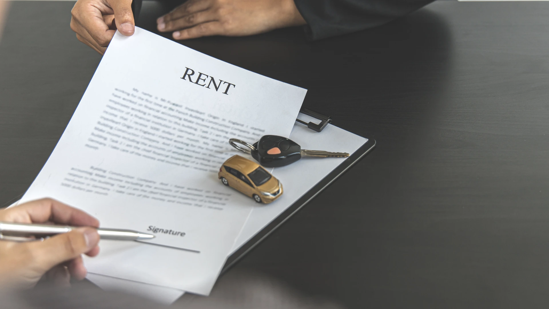 Hands signing a rent agreement with car keys and a toy car on a clipboard.