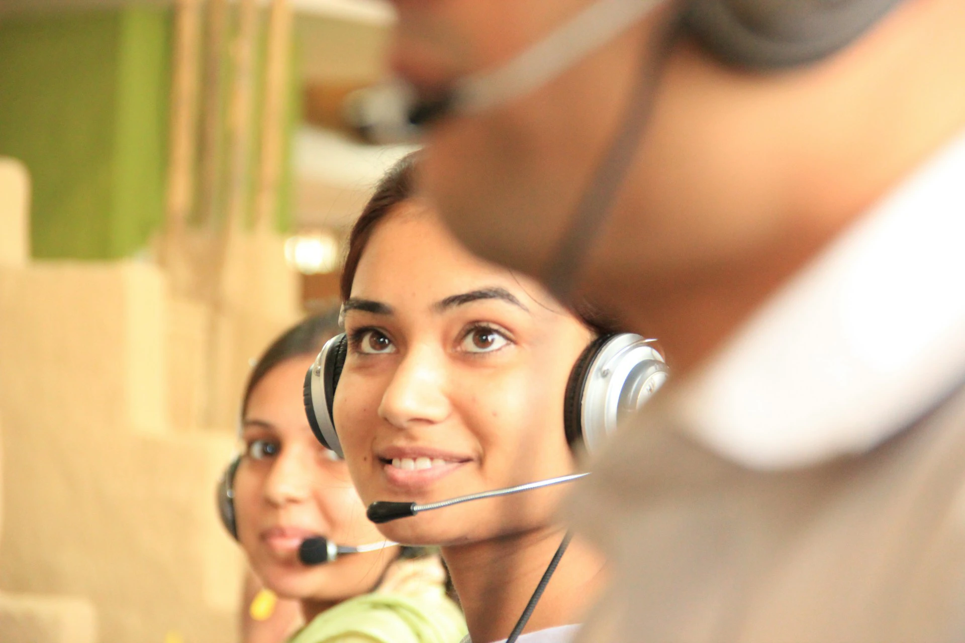 Three women wearing headsets with microphones are in a call center.