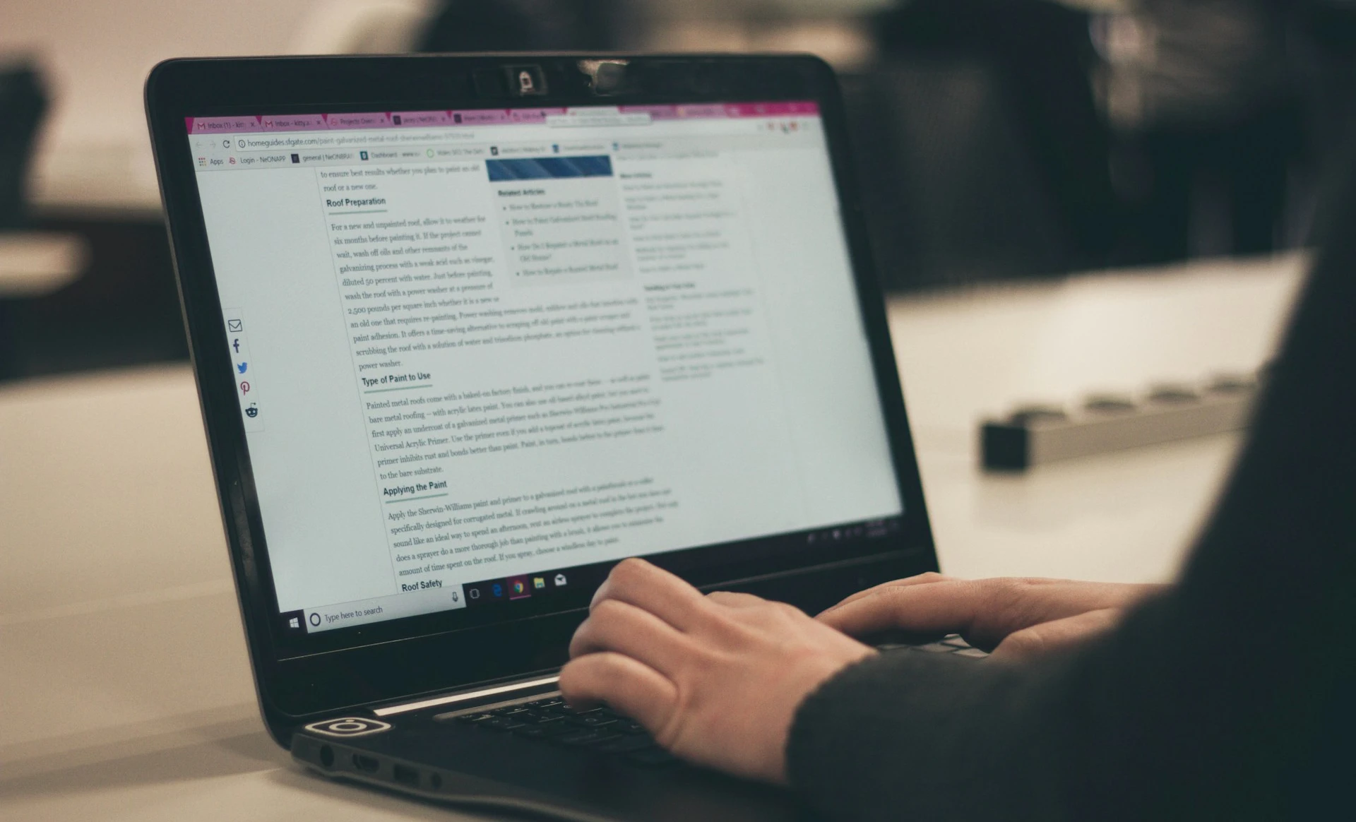 Person's hands typing on a laptop displaying a webpage with text.
