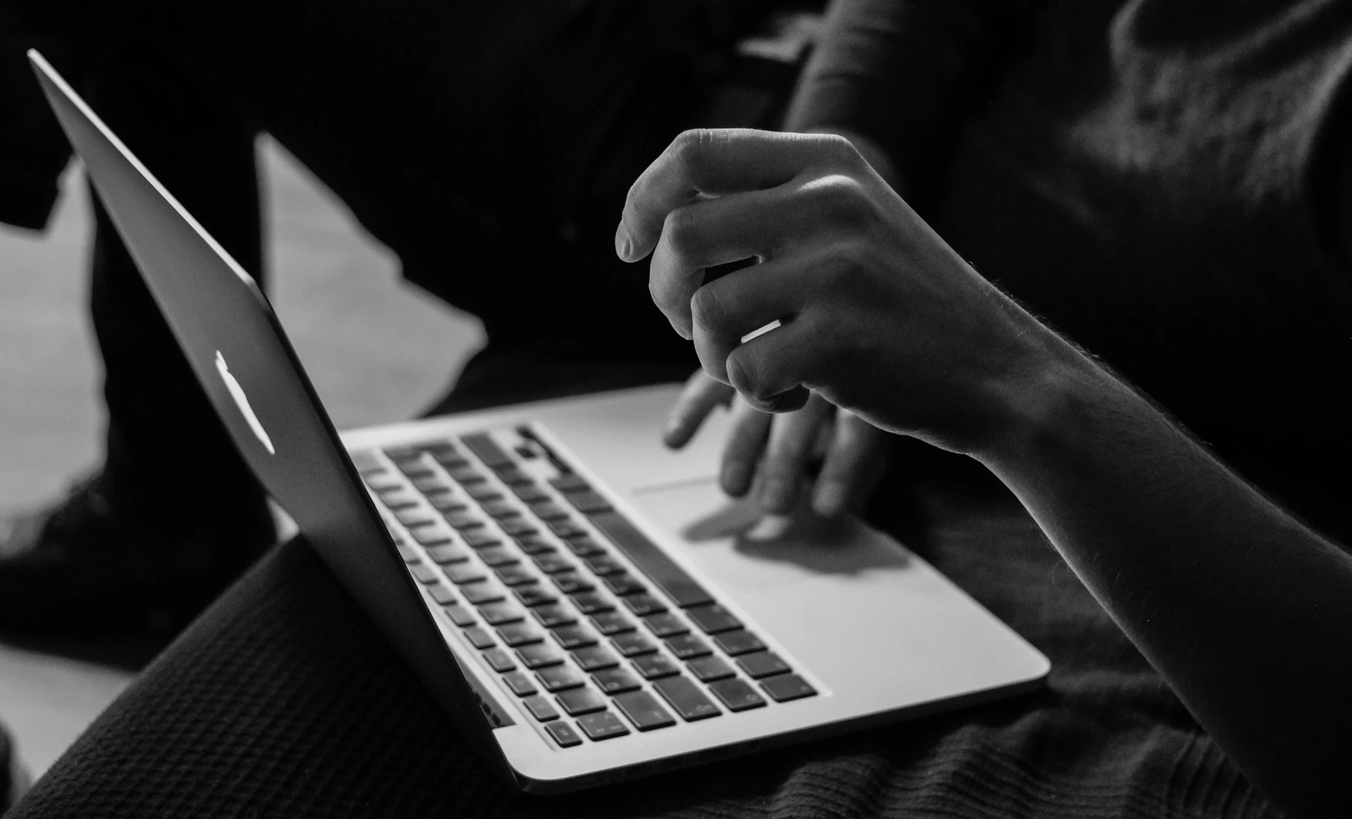 Person typing on a laptop in a dimly lit setting, captured in black and white.