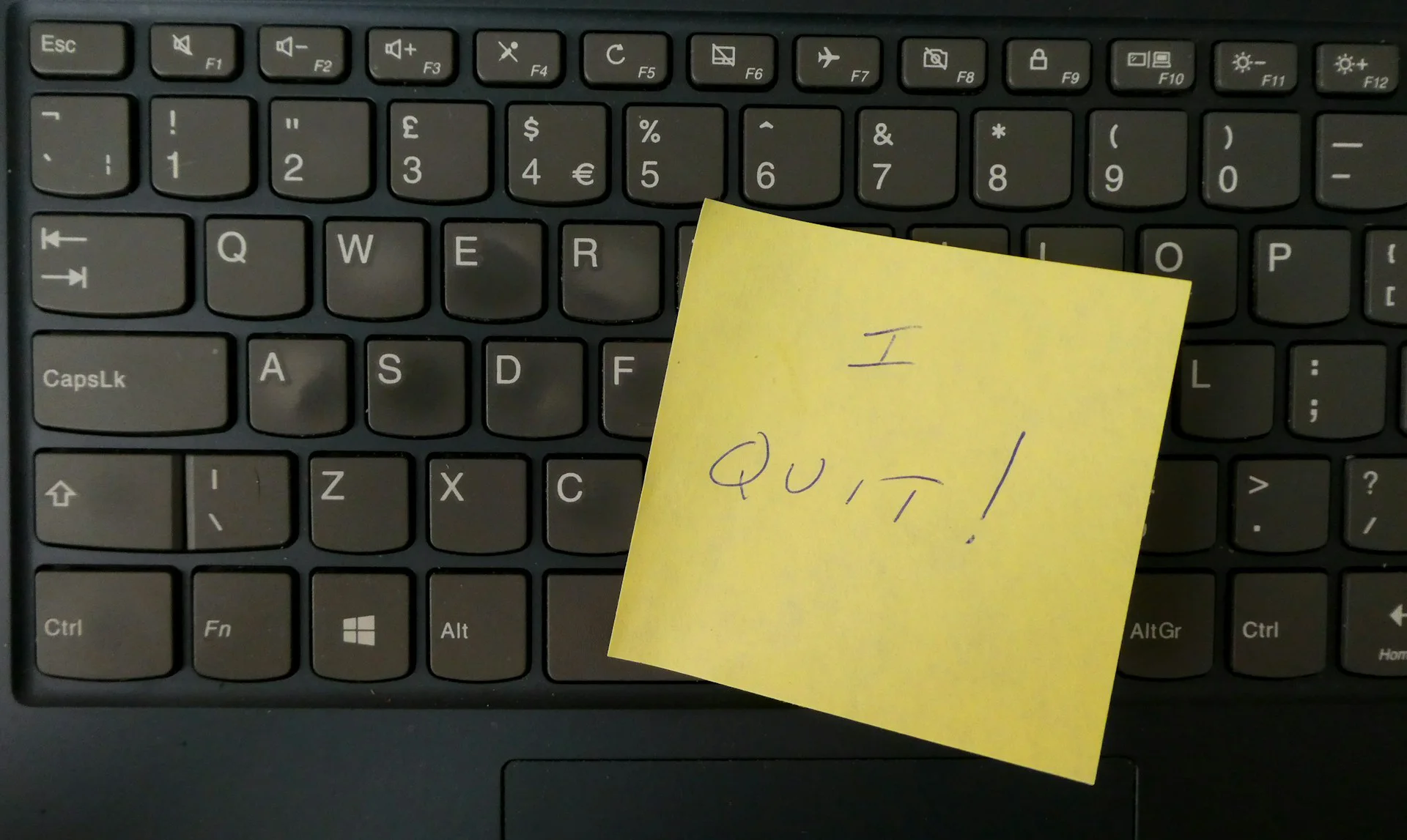 Yellow sticky note handwritten “I quit!” placed on a black computer keyboard.